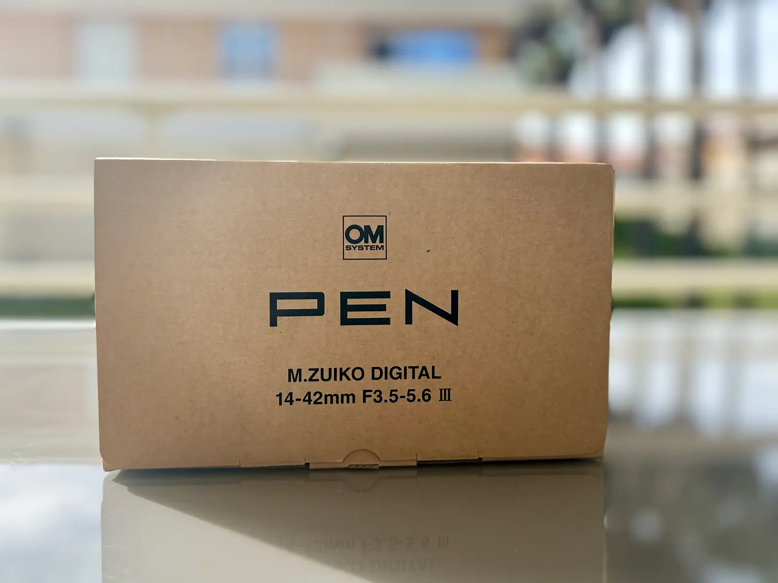 Carton brut imprimé du kit OM SYSTEM PEN et de son objectif 14–42 mm